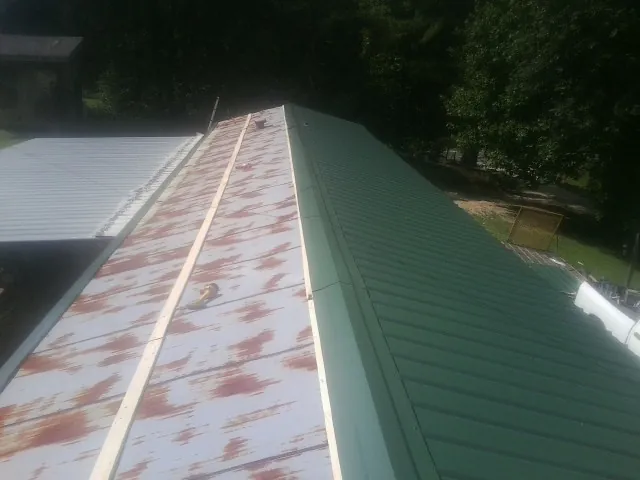 Old rusted panels beside newly installed green metal roofing — Wind Damage Roof Repair by Roofing Brothers in Corning