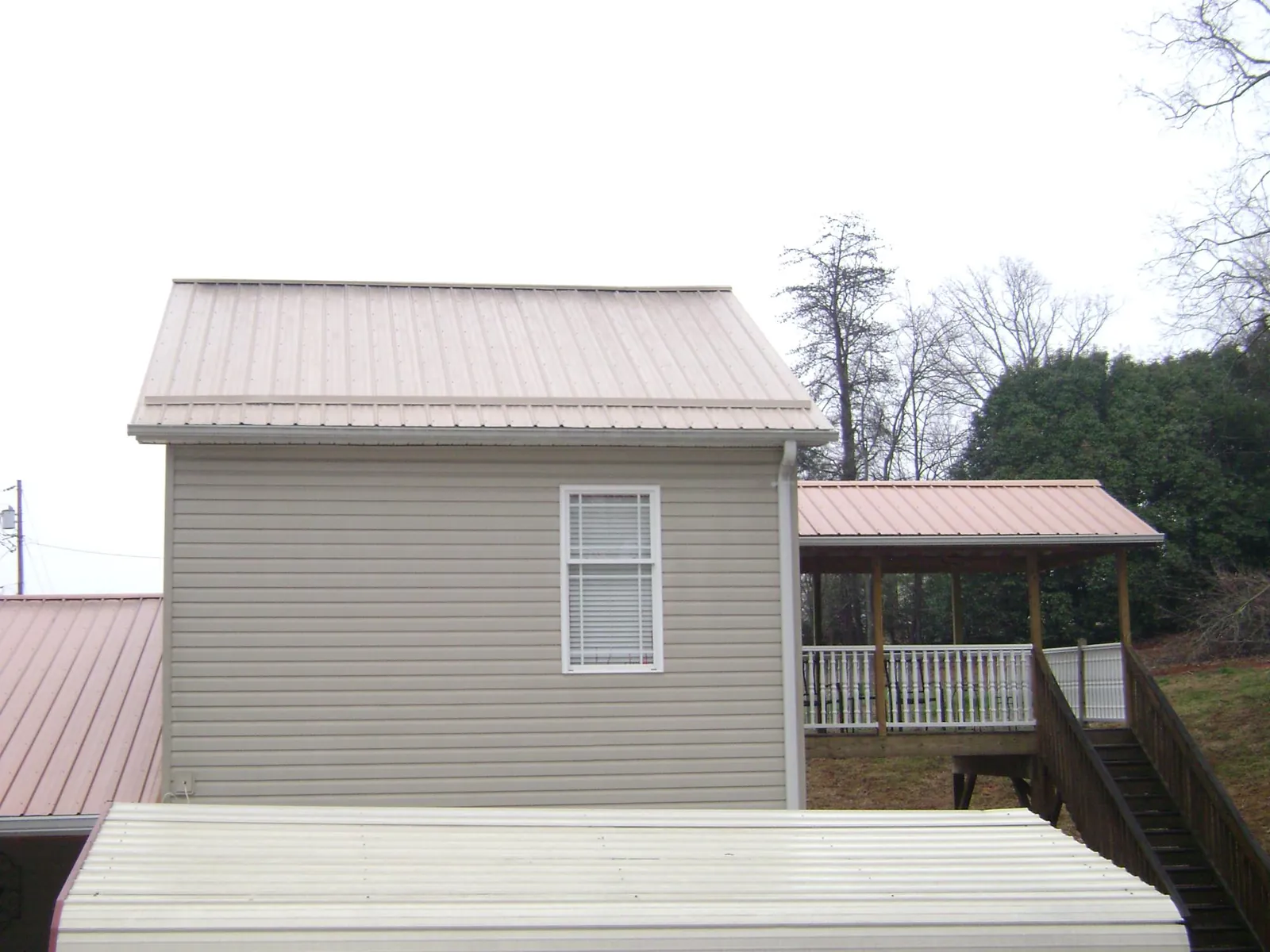Tan metal roofs on a two story addition and attached porch, from a Roof Replacement job in Corning